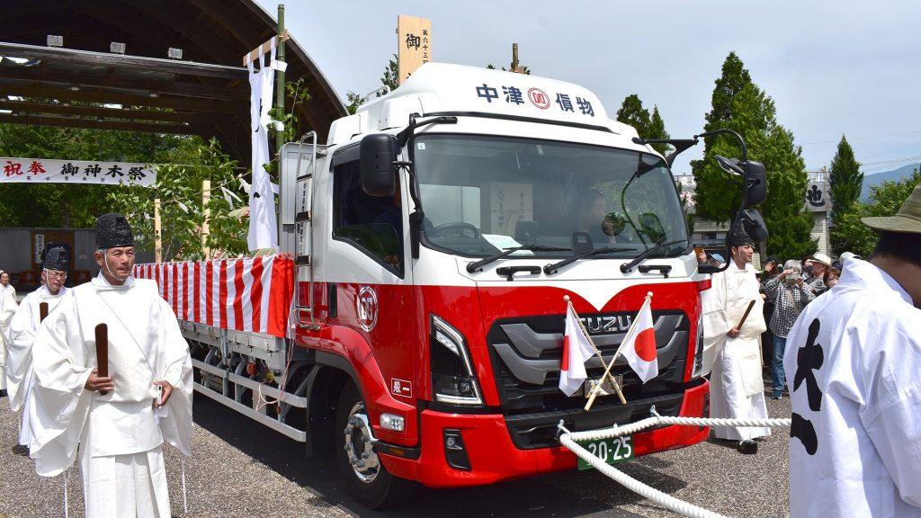 御神木を牽引する、紅白幕と国旗の旗が装飾されたトラック